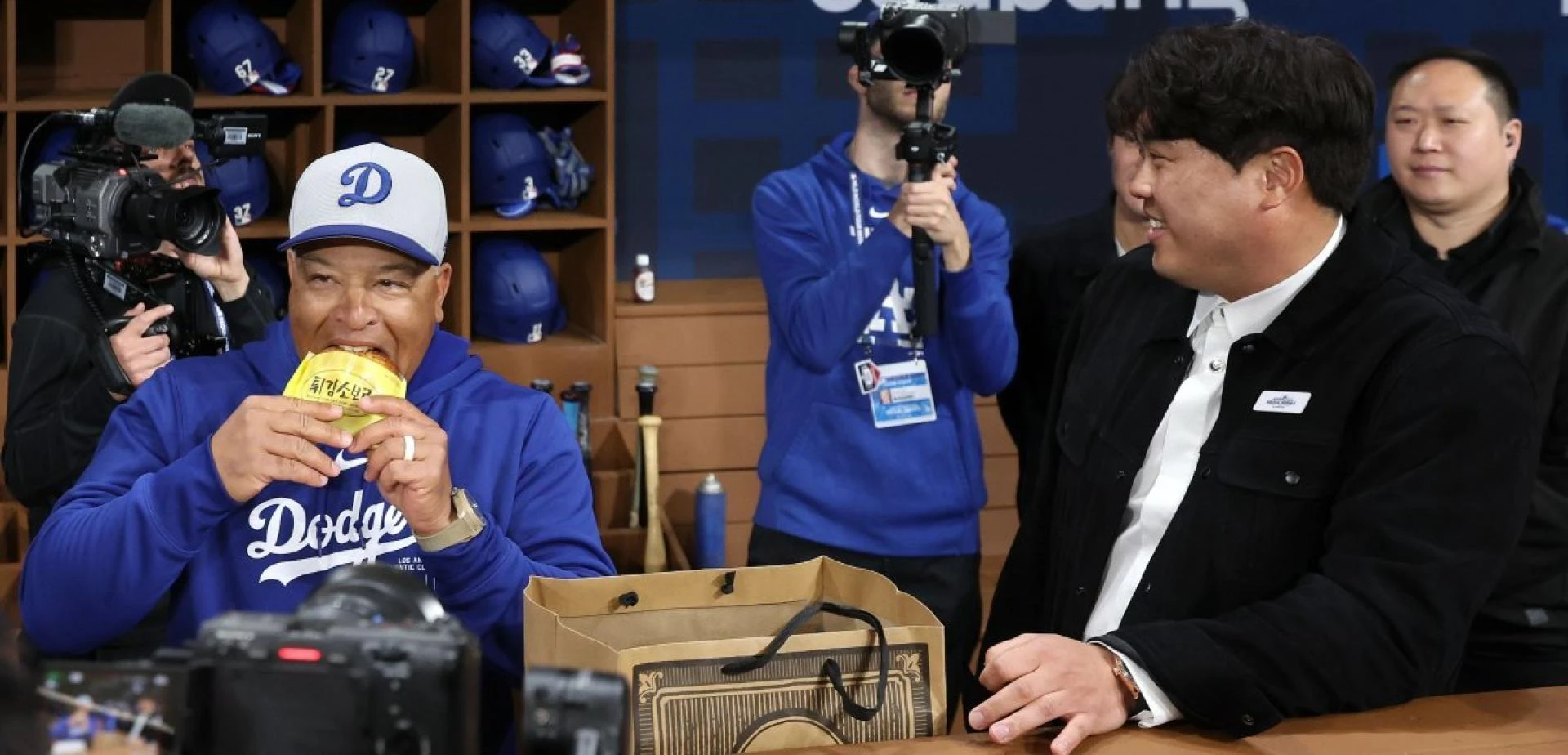 Los Angeles Dodgers manager Dave Roberts (left) is biting into a fried soboro bread gifted by Ryu Hyun-jin ahead of the American professional baseball Major League opening game against San Diego held at Gocheok Sky Dome in Seoul on the 20th. Newsis