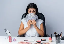 Screenshot 2023-08-14 at 18-25-09 Free Photo Beautiful woman sits at table with makeup tools covered face with cash