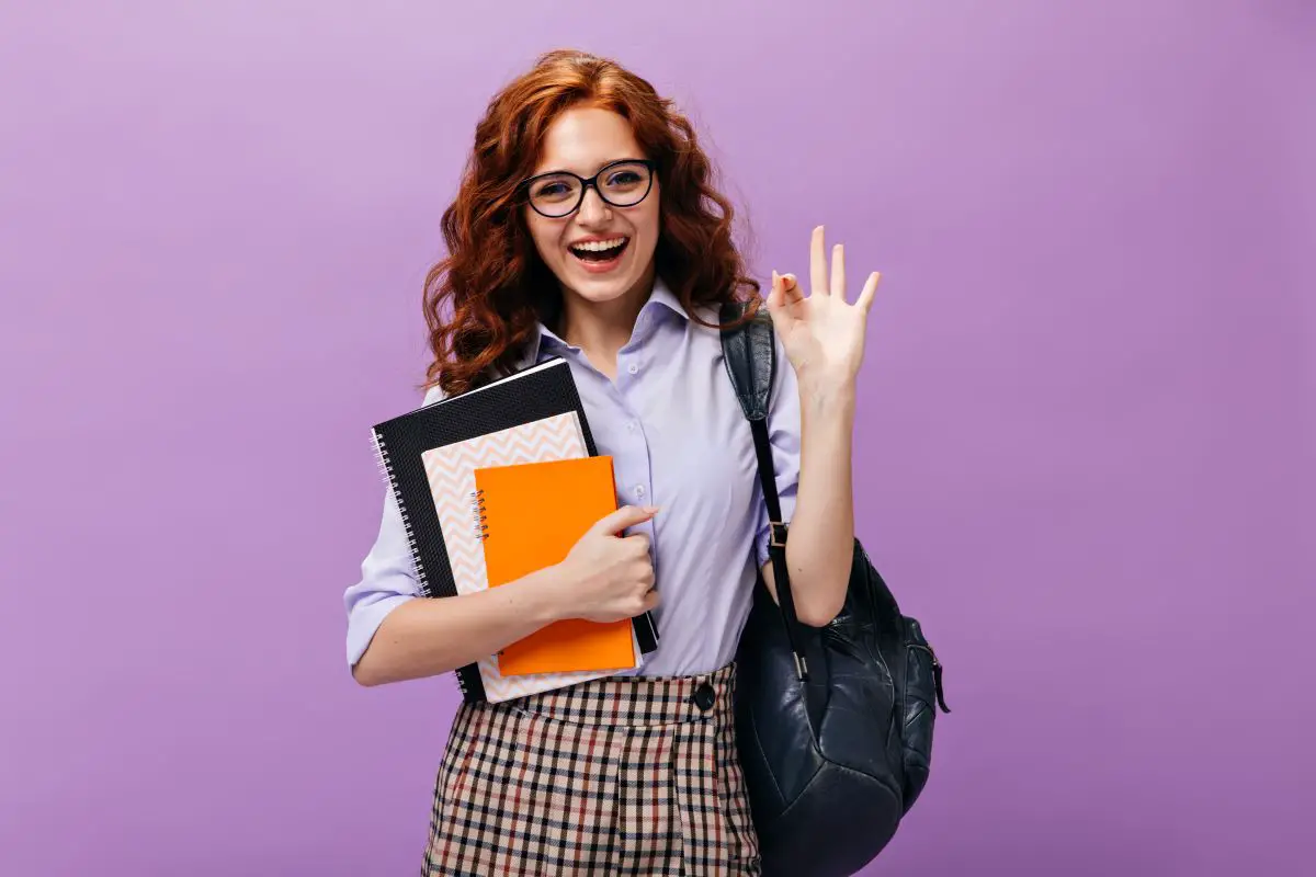 red-haired-lady-eyeglasses-holds-books-shows-ok-sign1