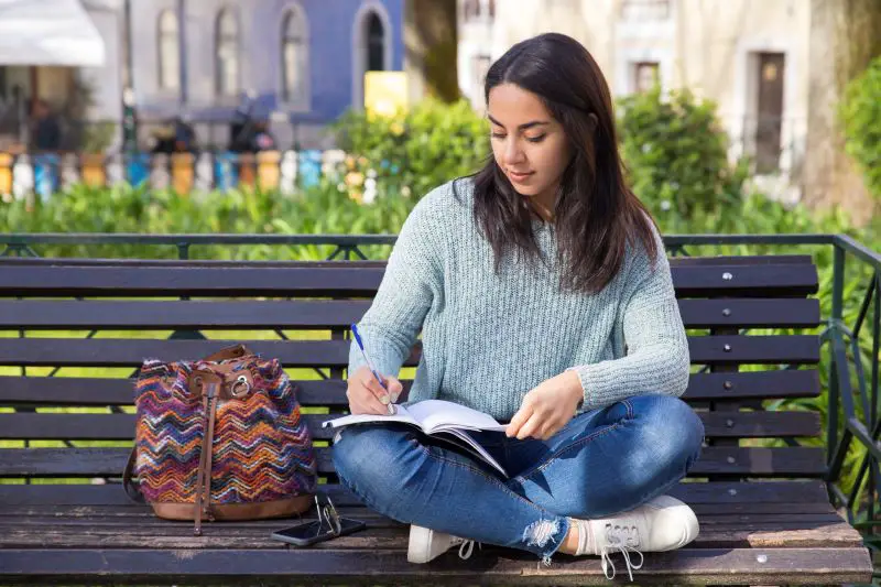 serious-woman-making-notes-sitting-bench-outdoors..